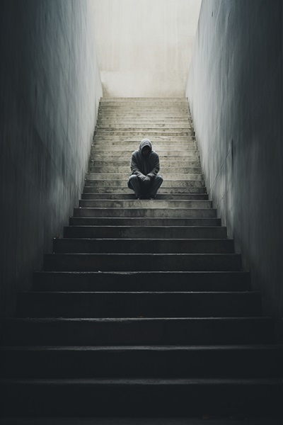 Auf einer langen Treppe, zwischen zwei hohen Wänden sitzt weit oben eine einzelne Person ganz alleine.