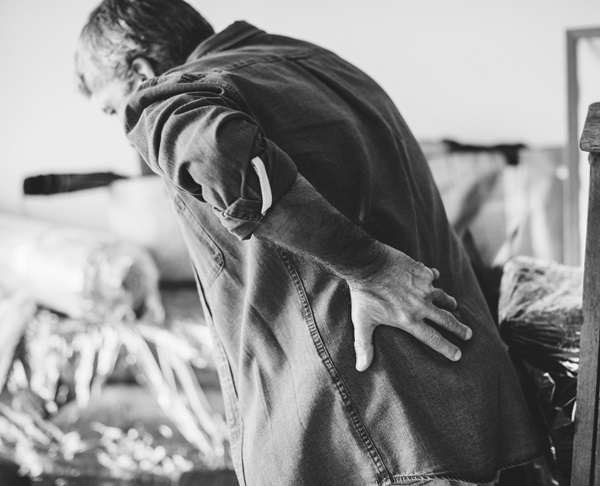 Ein älterer Mann steht vornübergebeugt und hält seine Hand im Rücken.