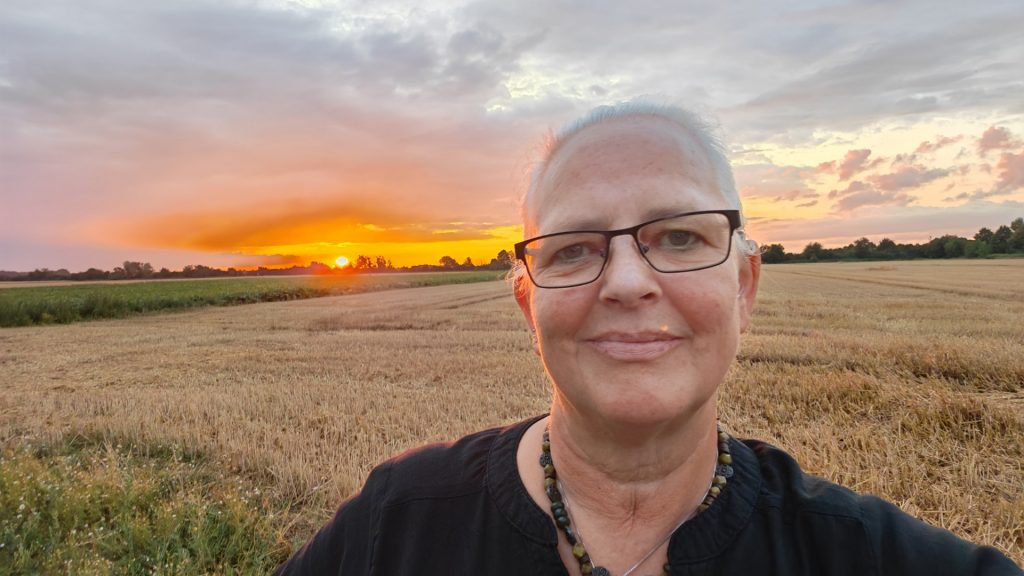 Alexandra steht vor einem gelben Weizenfeld im roten Sonnenuntergang