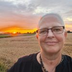 Alexandra steht vor einem gelben Weizenfeld im roten Sonnenuntergang