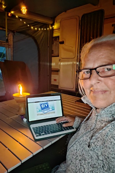 Alexandra sitzt im Vorzelt ihres Wohnwagens und schreibt an diesem Blog-Artikel. Hinter ihrem Tablet sieht man eine Kerze leuchten.