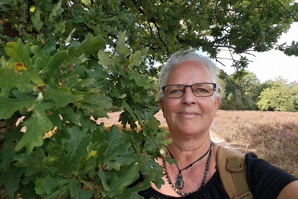 Alexandra steht auf einer Wiese, direkt neben hier hängt ein Ast einer Eiche herab und die Blätter schmiegen sich an ihr Gesicht.