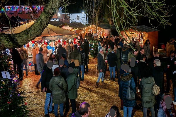 Ein Weihnachtsmarkt in Krefeld am 29.11.2025. Man sieht mehrere weihnachtlich geschmückte Holzbuden und viele Menschen, die sich auf dem Platz in der Mitte, der mit Stroh ausgelegt ist, unterhalten, herum gehen, und gemeinsam die weihnachtliche Stimmung genießen.