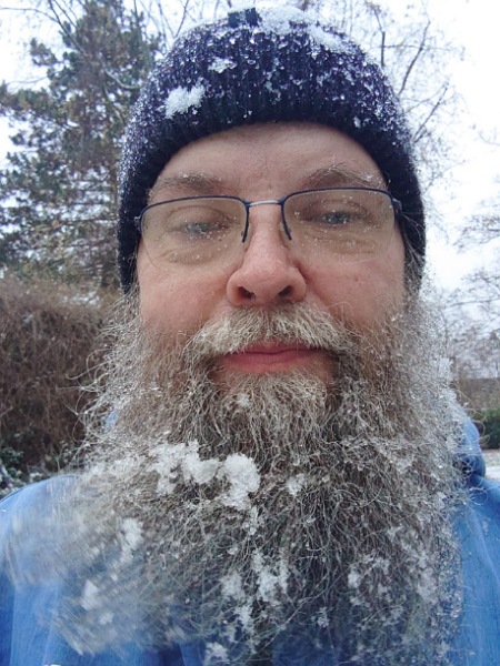 Rainer, der Partner von Alexandra Winkens, mitten im Schnee. Die Mütze ist bedeckt mit dicken Schneeflocken, und auch in seinem langen, grauen Bart haben sich ganz viele Flocken gefangen.
