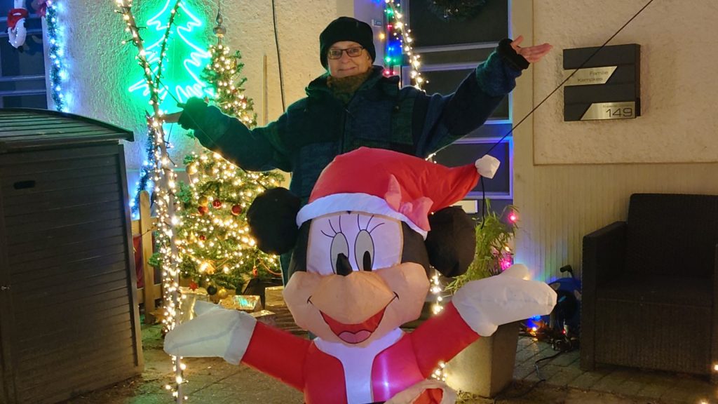 Titelbild für den Blogartikel Monatsrückblick 2025 von Alexandra Winkens. Alexandra steht hinter einer mit Luft gefüllten, weihnachtlich beleuchteten Mickey Mouse. Beide haben die Arme zu den Seiten ausgebreitet. Drum herum sind viele Weihnachtslichter zu sehen.