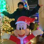 Titelbild für den Blogartikel Monatsrückblick 2025 von Alexandra Winkens. Alexandra steht hinter einer mit Luft gefüllten, weihnachtlich beleuchteten Mickey Mouse. Beide haben die Arme zu den Seiten ausgebreitet. Drum herum sind viele Weihnachtslichter zu sehen.