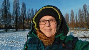 Beitragsbild zum Blogartikel "Monatsrückblick Januar2026". Alexandra steht, dick in Winterklamotten eingepackt auf einer mit Schnee bedeckten Wiese und lässt sich die Sonne ins Gesicht scheinen.